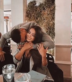 a man is kissing a woman at a table with drinks and silverware on it