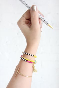 a woman's arm with three bracelets on it and a pen in the other hand