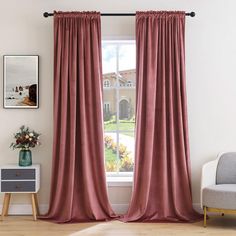 a living room with a chair and window covered in pink draping next to a potted plant