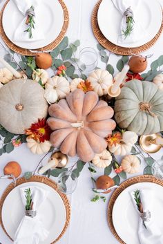 the table is set with white plates and pumpkins