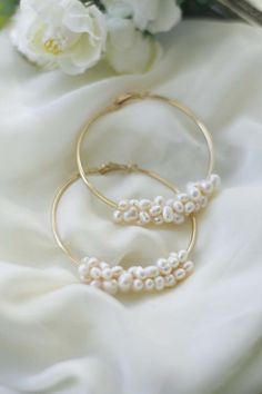 two bracelets with pearls are laying on a white cloth next to flowers and scissors