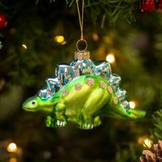 an ornament shaped like a dinosaur hanging from a christmas tree with lights in the background