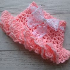 a pink crochet hat with a white bow on it sitting on a wooden surface