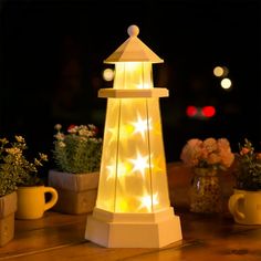 a white lighthouse shaped light on top of a wooden table next to potted plants