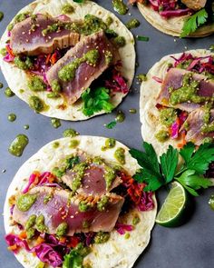 three tortillas topped with meat and veggies next to a lime wedge