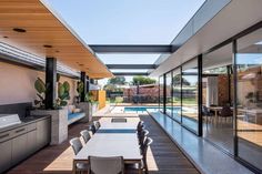 an outdoor dining area with table and chairs next to the swimming pool is surrounded by glass walls