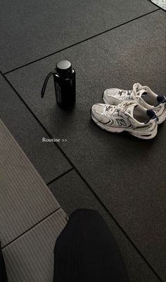 a pair of white sneakers sitting on top of a floor next to a black cup