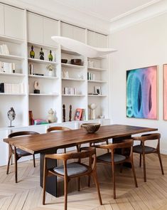 a dining room table and chairs in front of bookshelves with art on the wall