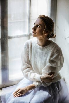 a woman sitting in front of a window with her hands on her hips and looking up