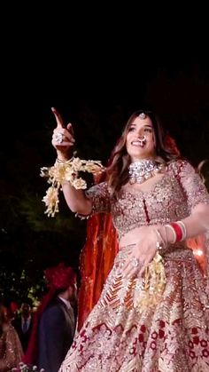 a woman in a red and gold wedding dress is dancing with her hands out to the side