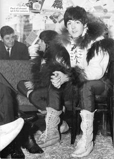 an old black and white photo of two people sitting on a couch, one wearing boots