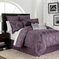 a bed in a bedroom with purple comforter and pillows