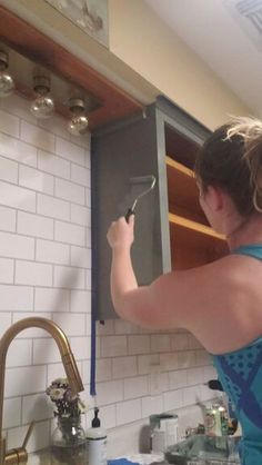 a woman in a blue top is cleaning the kitchen sink with a rag and sprayer