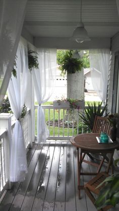 the porch is covered with white curtains and has a wooden table on it, along with potted plants