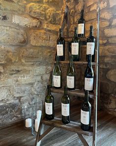 several bottles of wine are arranged on a wooden stand in front of a stone wall