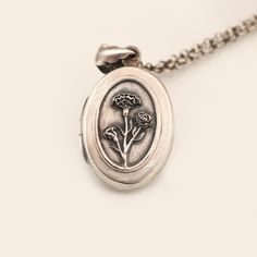 "Birth month flower locket necklace in 925 sterling silver with a working compass inside and a place for your favorite photo. One of January's birth flower is a carnation.  Depending on its color carnations can indicate many nuances of love, like a mother's love, admiration, remembrance, or deep unyielding love. Those born in January are thoughtful and wise in all matters of the heart. This lovely sterling silver oval locket features a lovely group of carnations on the front. The locket has been Sterling Silver Locket Necklace Gift For Mom, Sterling Silver Locket Necklace For Mom, Sterling Silver Locket Necklace With Flower Pendant, Sterling Silver Flower Pendant Locket Necklace, Flower Charm Locket Necklace Keepsake, Silver Locket Necklace With Birth Flower For Anniversary, Silver Flower Jewelry For Memorial, Vintage Birth Flower Medallion Jewelry, Vintage Medallion Jewelry With Birth Flower