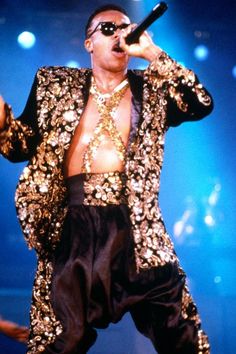 a man in a gold and black suit on stage with his arms out to the side