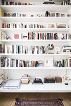 a bookshelf filled with lots of books next to a white desk and chair