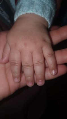 a close up of a person holding a baby's hand with both hands on top of each other