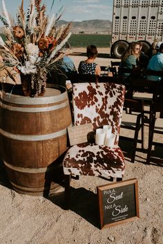 a cow print chair sitting in front of a barrel filled with flowers and other items