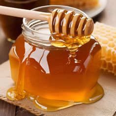 a jar of honey with a wooden spoon in it and some honeycombs on the table