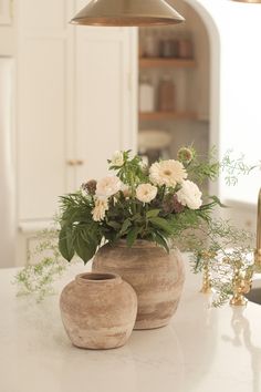 two vases with flowers in them sitting on a kitchen counter next to a lamp