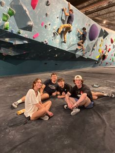 four people sitting on the ground in front of a climbing wall