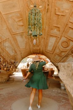 a woman in a green dress and hat walking through a tunnel with chandeliers hanging from the ceiling