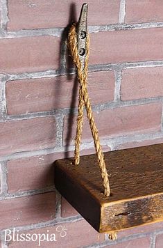 a wooden shelf with rope hanging from it's sides against a red brick wall