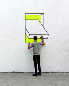 a man holding up a drawing on the side of a wall with yellow and black lines