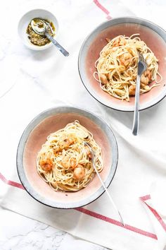 two bowls filled with pasta and shrimp on top of a white table cloth next to silverware