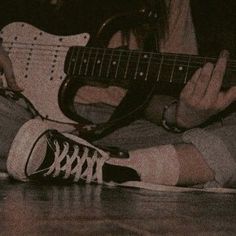 a person sitting on the floor with a guitar in their lap and one hand holding an electric guitar