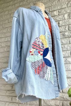 a blue jean jacket with colorful patches on the front and back, hanging from a mannequin's dummy