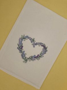 an embroidered heart on a white piece of paper with purple flowers in the shape of a heart