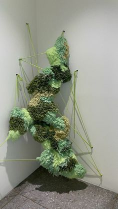 a sculpture made out of green and yellow yarn on the ground next to a white wall