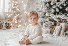 a little boy sitting in front of a christmas tree