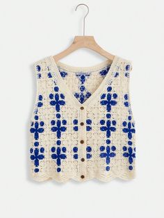 a white and blue knitted vest hanging on a wooden hanger with an embroidered cross pattern