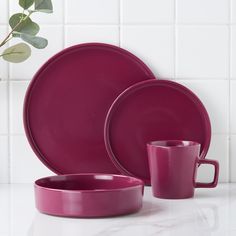 a set of pink dinnerware on a white countertop next to a potted plant