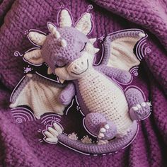 a crocheted dragon laying on top of a purple blanket