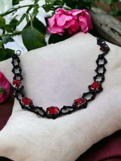 This elegant choker, perfect for Victorian or gothic attire, features a striking design of black and deep red. It showcases five deep red oval crystals, each separated by delicate black seed beads, adding to its intricate allure. The necklace measures 11 inches in length, with an adjustable 3-inch extension chain for a customizable fit. This piece is both dramatic and sophisticated, making it an ideal accessory for those seeking to make a bold statement. The versatility of the gothic choker know Gothic Red Necklace For Cosplay, Red Gothic Necklace For Cosplay, Red Punk Choker As Gift, Adjustable Black Fantasy Choker, Red Emo Choker Jewelry, Red Emo Style Choker Jewelry, Black Fantasy Style Choker As Gift, Black Fantasy Choker As A Gift, Black Fantasy Style Choker For Gift