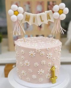 a pink cake decorated with white flowers and balloons