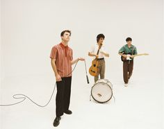 three young men are playing instruments and singing in front of a white background while standing next to each other