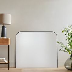 a table with a lamp and vase on it next to a white board that is leaning against the wall