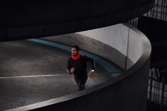 a man in black jacket and red scarf running on concrete path next to large building