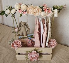 a wooden crate filled with pink and white flowers on top of a bed next to a stuffed animal