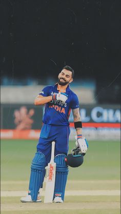 a man standing on top of a field holding a cricket ball and batting helmet in his hand