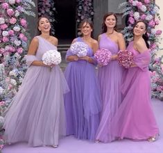 four bridesmaids standing in front of a floral arch holding bouquets and flowers