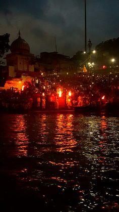 a group of people sitting on the side of a body of water with lit candles in front of them