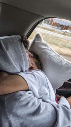 a man sleeping in the back seat of a car with his arms wrapped around him