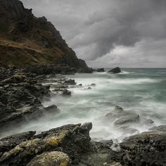 the rocky shore is covered in water and rocks under a cloudy sky with dark clouds